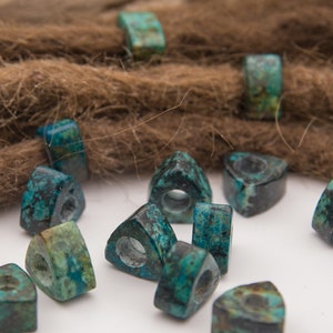 May include: A close-up of turquoise triangle-shaped beads with a hole in the center. The beads are scattered on a white surface.