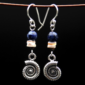 Puede incluir: Un par de pendientes de plata con cuentas azules y blancas y un dije de amonita de plata.