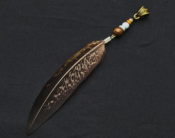 May include: A brown and black feather with a decorative metal and wooden bead accent. The feather is attached to a metal clasp.