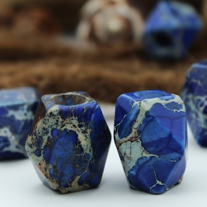 Puede incluir: Primer plano de seis cuentas de piedra preciosa marmoleadas azules y blancas. Las cuentas son facetadas y tienen forma hexagonal.