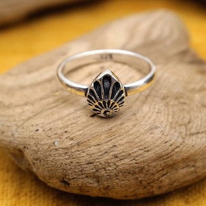 Peut inclure: Une bague en argent avec un motif en forme de larme noir et argent. La bague est posée sur un morceau de bois flotté.