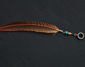 May include: A brown and black pheasant feather with a turquoise bead, a brown bead, and a silver ring attached to the end.