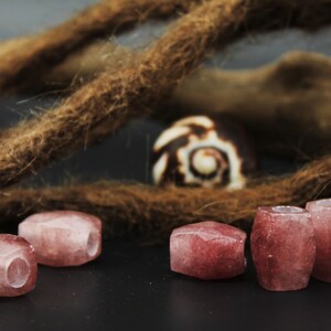May include: Five pink and white gemstone beads with a hole through the center. The beads are arranged in a row on a dark surface.