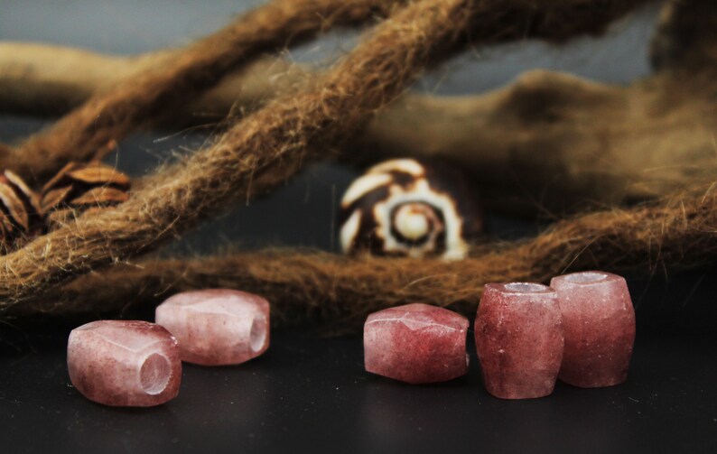 May include: Five pink and white gemstone beads with a hole through the center. The beads are arranged in a row on a dark surface.