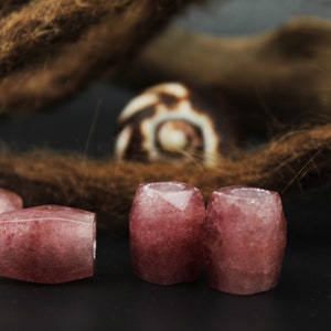 May include: Four pink and white gemstone beads, each with a faceted, rectangular shape. The beads are arranged in a row on a dark surface.
