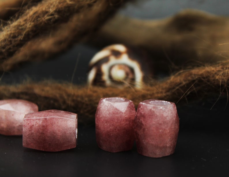 May include: Four pink and white gemstone beads, each with a faceted, rectangular shape. The beads are arranged in a row on a dark surface.
