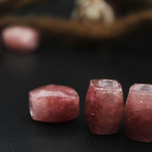 May include: Three pink and white gemstone beads with a faceted, rounded shape. The beads are arranged in a row on a black surface.