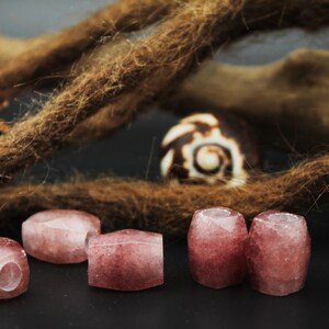 May include: Five pink and white gemstone beads with a hole through the center. The beads are arranged in a row on a dark surface.