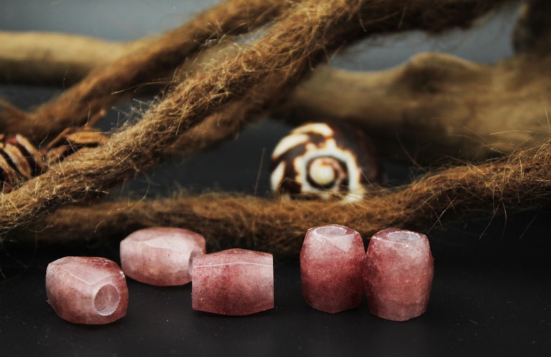 May include: Five pink and white gemstone beads with a hole through the center. The beads are arranged in a row on a dark surface.
