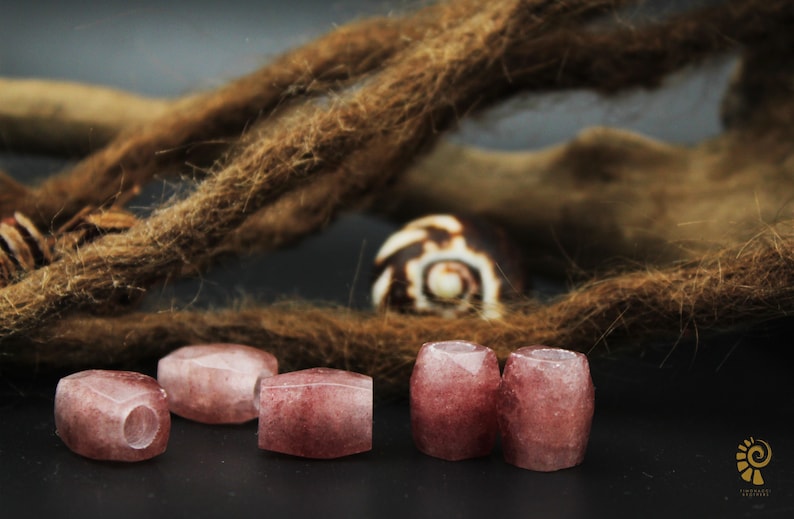 May include: Five pink and white gemstone beads with a faceted finish. The beads are arranged in a row on a dark surface.