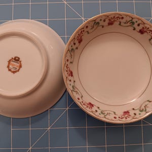 May include: Two white ceramic bowls with a gold rim. One bowl shows the interior with a floral scroll pattern in red and green. The other bowl is flipped over to show the base with a stamp that reads Berkshire Imperial China in the center.