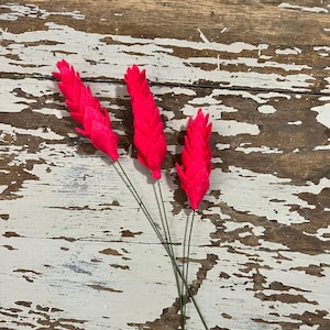 May include: Three bright pink felt flower stems with green wire stems. The flowers are arranged in a fan shape.