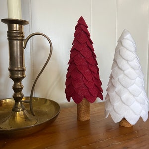 May include: Two felt Christmas trees, one red and one white, with cork bases. The trees are decorated with felt leaves.
