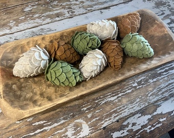 May include: A wooden bowl filled with felt pine cones in shades of green, brown, and beige. The pine cones are handmade and have a rustic, natural look.