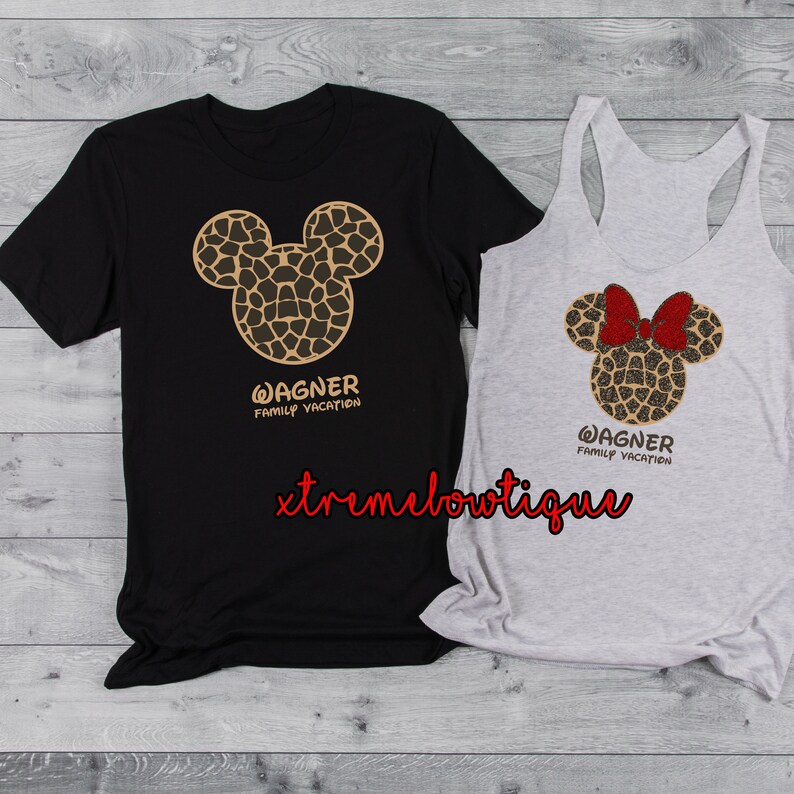 Może przedstawiać: Czarny t-shirt i szary top na ramiączkach z nadrukiem brązowej i złotej głowy Myszki Miki. Głowa Myszki Miki ma czerwoną kokardkę na topie na ramiączkach. Tekst "WAGNER FAMILY VACATION" jest nadrukowany pod głową Myszki Miki na obu koszulkach.