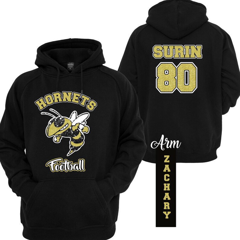 Puede incluir: Sudadera con capucha negra con un gr&aacute;fico dorado y blanco de Hornets Football en la parte delantera. La parte trasera presenta el nombre "SURIN" y el n&uacute;mero "80" en dorado. Una etiqueta vertical en el brazo dice "ZACHARY".