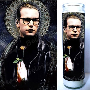 Könnte beinhalten: Eine weiße Glaskerze mit einem Schwarzweißbild eines Mannes mit Brille, der eine Blume hält. Der Mann trägt eine schwarze Jacke und einen schwarzen Rollkragenpullover. Die Kerze hat ein weißes Etikett mit den Worten "Lieber Geliebter" darauf.