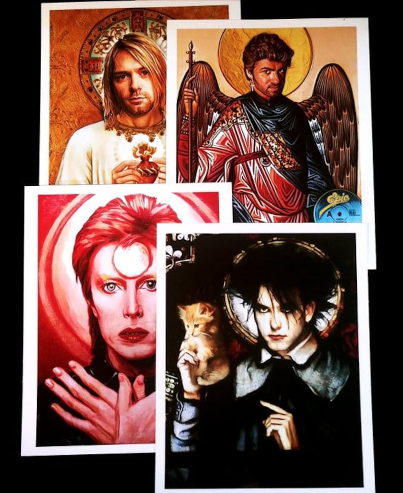 May include: Four different art prints featuring portraits of musicians. The first print features a man with long blonde hair wearing a white shirt and holding a red heart. The second print features a man with long brown hair wearing a red and gold robe with angel wings. The third print features a man with red hair wearing a black shirt and a white halo. The fourth print features a man with black hair wearing a black shirt and holding a small orange cat.