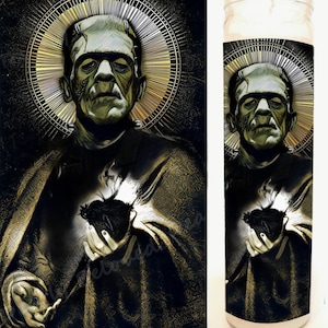 Op de afbeelding: Een zwarte en gouden kaars met een afbeelding van Frankenstein die een hart vasthoudt. De kaars zit in een glazen pot met een wit etiket.