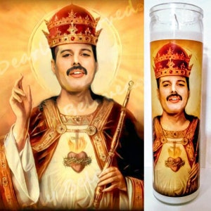 Op de afbeelding: Een kaars met een afbeelding van Freddie Mercury, gekleed als een koning, met een kroon, een gewaad en een hart met vlammen. De kaars is wit met een doorzichtige glazen houder.