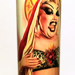 May include: A white candle with a colorful image of a person wearing a red robe and a gold crown. The person has a large heart with flames on their chest. The image is surrounded by a yellow halo.