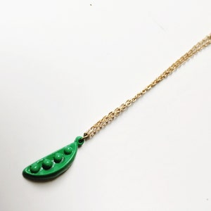 May include: A gold chain necklace with a green pea pod charm. The charm has four green peas inside.
