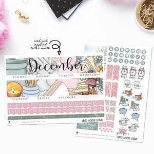May include: A December calendar planner with a winter-themed design featuring a cheese board with various cheeses, crackers, and olives. The calendar has a pink and green color scheme with gold accents. The planner includes stickers with various designs, including coffee cups, clocks, and money bags.