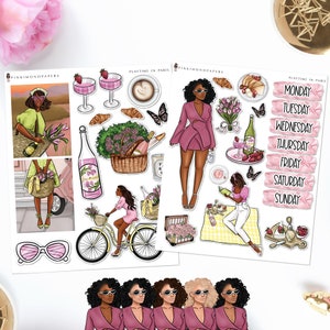 Puede incluir: Dos hojas de pegatinas con ilustraciones de un picnic en París. Una hoja presenta a una mujer con un vestido rosa, una bicicleta y una botella de champán. La otra hoja tiene etiquetas de días de la semana e ilustraciones de cruasanes y bebidas.