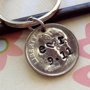 May include: A silver keychain with a dime pendant. The dime is stamped with the words "e <3 r 9.11 2003". The keychain is attached to a silver key ring. The background includes a vintage key and a floral pattern.