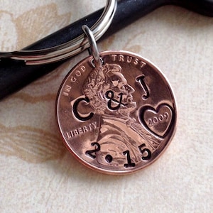 May include: A copper penny keychain with the initials "C & J", a heart with "2009", and the date "2.15" engraved. The keychain includes a silver key ring and a small metal loop. The penny is attached to the key ring.