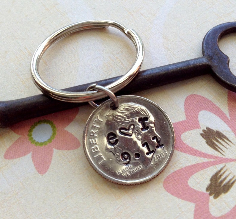 May include: A silver keychain with a dime pendant. The dime is stamped with the words "e <3 r 9.11 2003". The keychain is attached to a silver key ring. The background includes a vintage key and a floral pattern.