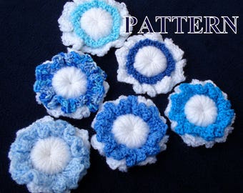 May include: Six crocheted flower embellishments in shades of blue and white. The flowers have a ruffled edge and a white center. The word "PATTERN" is written in black letters across the top of the image.