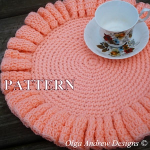 May include: A crocheted peach-colored coaster with a ruffled edge. The coaster is round and has a pattern of small circles. The word "PATTERN" is written in black letters on the coaster. The coaster is sitting on a wooden surface.