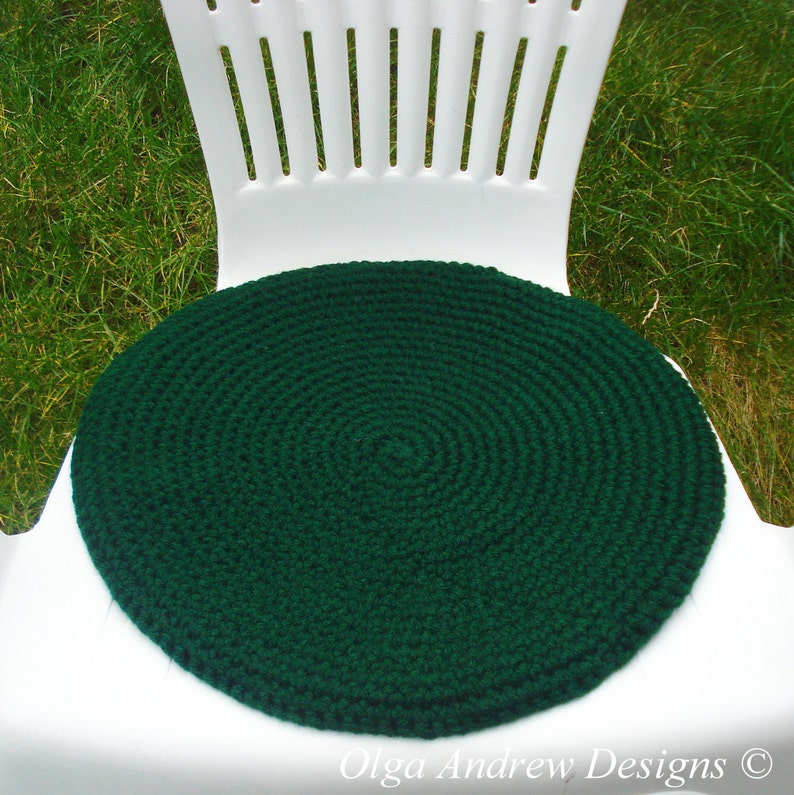 May include: A dark green crocheted round chair cushion. The cushion is made with a circular pattern and is sitting on a white chair.