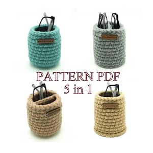 May include: Crochet pattern PDF for five different versions of a glasses holder. The holders are made in beige, gray, and teal yarn. Each holder has a small brown leather label.