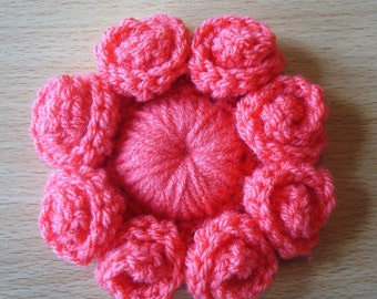 Puede incluir: Primer plano de una flor de ganchillo con ocho pétalos rosas y un centro rosa. La flor está hecha con punto bajo y tiene un aspecto texturizado. La palabra "PATTERN" está escrita en letras rojas sobre la flor.