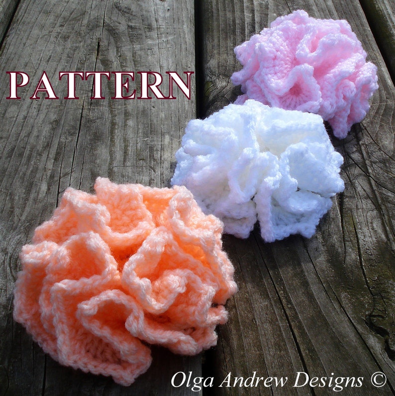 May include: Three crocheted flowers in different colors: peach, white, and pink. The flowers are arranged in a row on a wooden surface. The word "PATTERN" is written in red letters above the flowers.