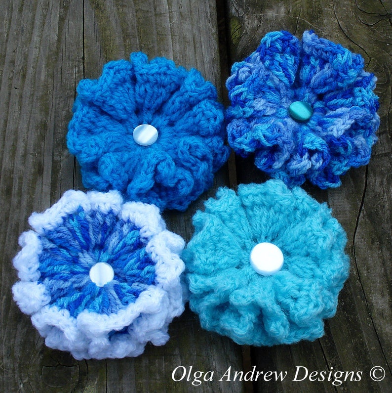 May include: Four crocheted flowers in shades of blue and white. Each flower has a white button in the center.