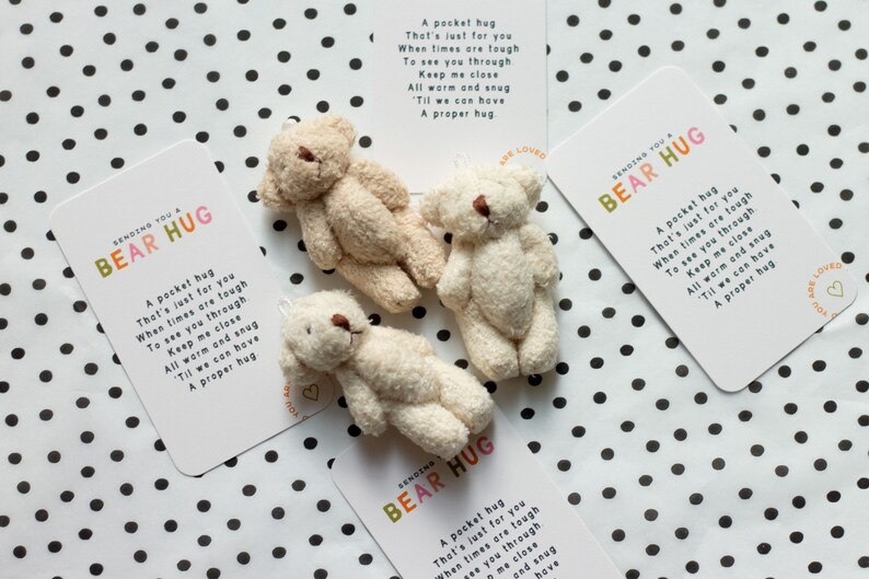 May include: Three small, cream-coloured teddy bears are arranged on a white background with black polka dots. Each bear is holding a card with the text "Sending you a Bear Hug" and a poem about a pocket hug.