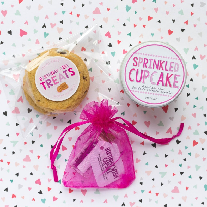 May include: A birthday gift set with a pink and white cupcake candle, a bag of chocolate chip cookies with a "Birthday Girl Treats" label, and a pink organza bag with a birthday wish capsule.