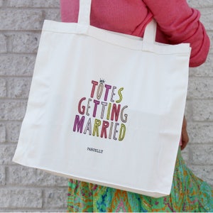 May include: White canvas tote bag with the text "Totes Getting Married" in colorful letters. The text is in a stacked, playful font. The bag has a black handle and the brand name "Parcelly" is printed in black at the bottom.
