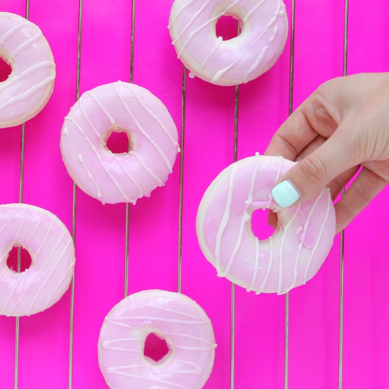 May include: Six pink and white frosted donuts with white icing and pink stripes on a pink wire rack.
