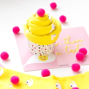 May include: A yellow cupcake-shaped sock gift with a pink pom-pom on top. The cupcake is sitting on a pink card with the text "Sweeter than a text" and the word "PARCELLY".
