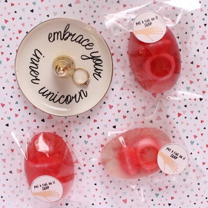 May include: Three red and white soap bars with the text "Put a ring on it soap" on a white background with pink and green hearts.