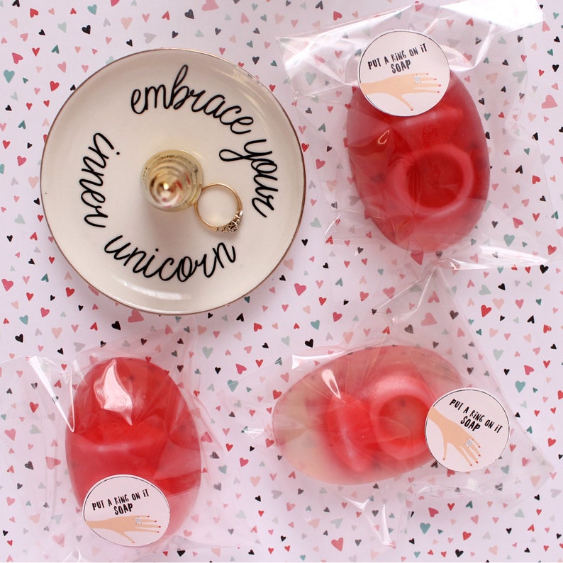 May include: Three red and white soap bars with the text "Put a ring on it soap" on a white background with pink and green hearts.