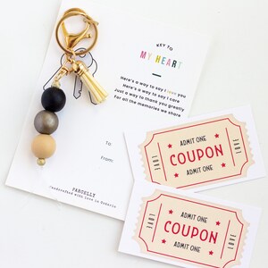 May include: A gold key chain with a black, gold, and beige beaded tassel. The keychain has a tag that says "Key to My Heart" and includes a coupon that says "Admit One Coupon Admit One".