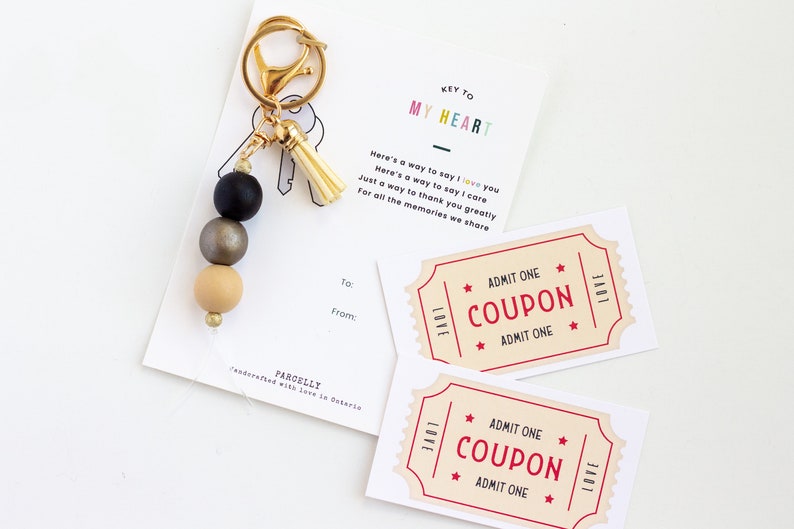 May include: A gold key chain with a black, gold, and beige beaded tassel. The keychain has a tag that says "Key to My Heart" and includes a coupon that says "Admit One Coupon Admit One".