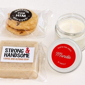 May include: A gift set featuring two chocolate chip cookies with a "For Him" sticker, a bar of coffee and almond soap, and a scented candle in a glass jar. The candle has a red label that says "Mandle".