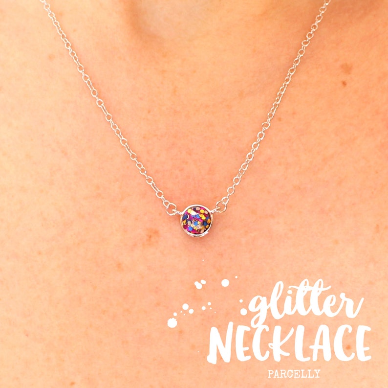 May include: A silver chain necklace with a small round pendant filled with colorful glitter. The pendant is about the size of a dime. The necklace is on a model's neck. The text "glitter necklace" is written in white letters on a white background below the image.