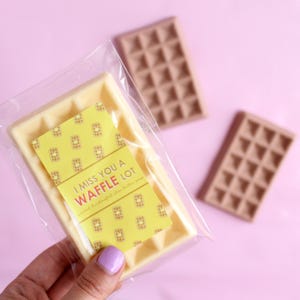 May include: A white waffle-shaped soap bar with a yellow label that reads "I miss you a waffle lot" and a waffle pattern. The soap is in a clear plastic bag.